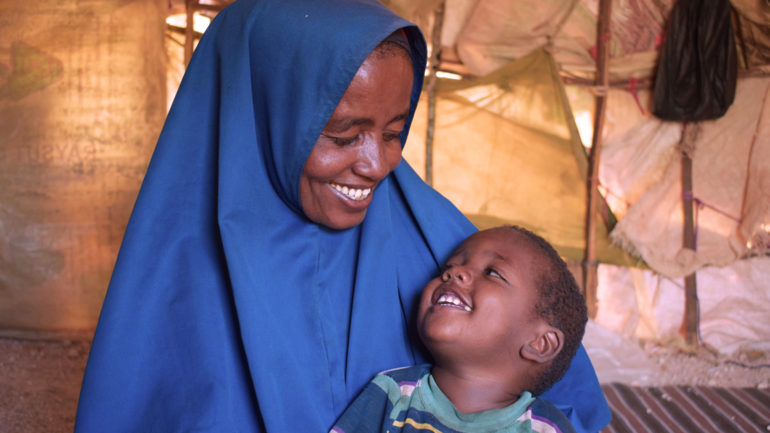 Freude schenken im Ramadan: Ihre Spende unterstützt Kinder und ihre Familien. Eine Mutter in blauem Hijab und ihr kleiner Sohn schauen sich lachend ins Gesicht