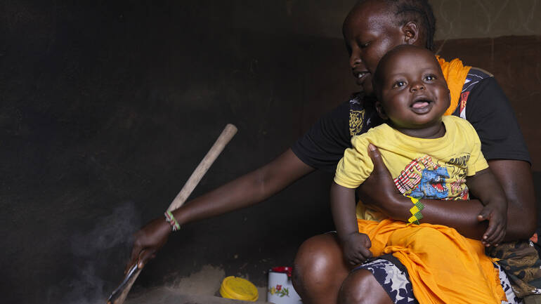 Gesunde Ernährung hilft Frauen, ihre Kinder stillen zu können. Agnes aus Kenia hält ihren Sohn Filex auf dem Arm, während sie sich eine gesunde Mahlzeit kocht.