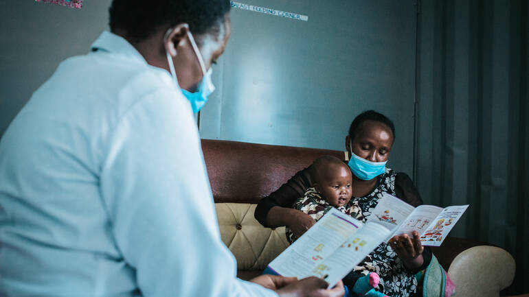 Im Stillraum im Krankenhaus Kapenguria in Kenia können Mütter ungestört ihre Kinder stillen und erhalten wertvolle Informationen. Ernährungsberaterin Miriam zeigt der Mitarbeiterin und Mutter Jane mit ihrem Kind die Vorteile des Stillens mit einem Flyer