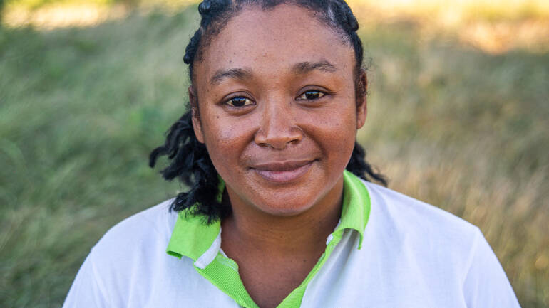 Lizà kümmert sich um die Ernährungssicherheit Lizà in ihrer Arbeitskleidung vor einem Feld.