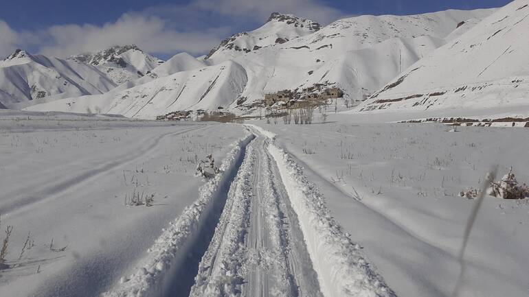 Vor allem in abgelegenen Gebieten sind im Winter viele afghanische Dörfer eingeschneit. Ein freigeschaufelter Weg durch den Schnee, im Hintergrund ein Dorf in Afghanistan.