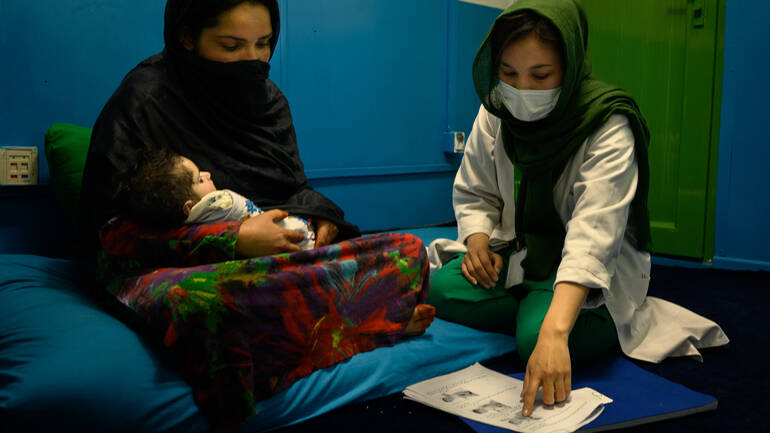 Eine Ernährungsberaterin zeigt einer jungen Mutter mit Baby auf dem Arm mehr zur richtigen und gut umsetzbaren Ernährung von Kleinkindern. Eine Ernährungsberaterin zeigt einer jungen Mutter mit Baby auf dem Arm mehr zur richtigen und gut umsetzbaren Ernährung von Kleinkindern.