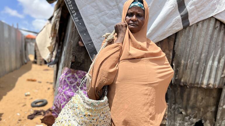 Faadumo trägt in orangenes Tuch gehüllt einen ihrer Körbe durch das Camp.