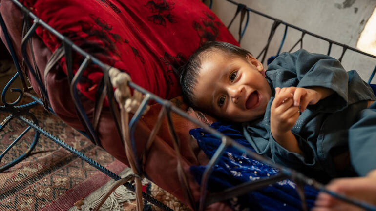 Arfanullah liegt in seinem Kinderbettchen und lacht fröhlich Arfanullah liegt in seinem Kinderbettchen und lacht fröhlich