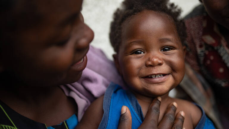 Ein kleines Mädchen aus der demokratischen Republik Kongo lacht in die Kamera, während es auf dem Schoß ihrer Schwester sitzt. Ein kleines Mädchen aus der demokratischen Republik Kongo lacht in die Kamera, während es auf dem Schoß ihrer Schwester sitzt.