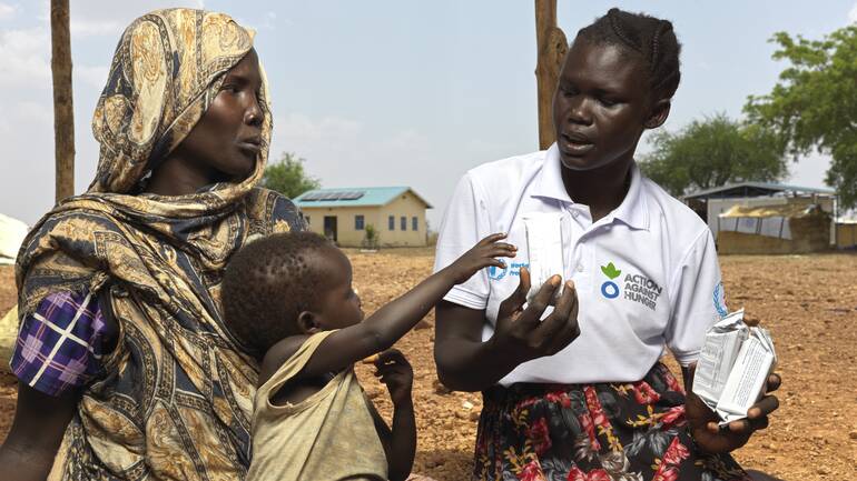 Eine Mitarbeiterin von Aktion gegen den Hunger gibt einer aus dem Sudan geflüchteten Mutter und ihrem Kind in einem Lager im Südsudan Tipps gegen Mangelernährung.