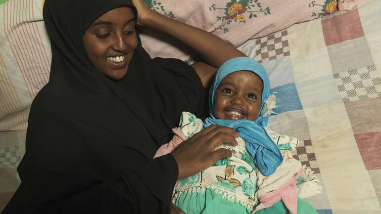 Medina und Munira liegen im Bett und kuscheln miteinander, beide sind sichtlich glücklich.