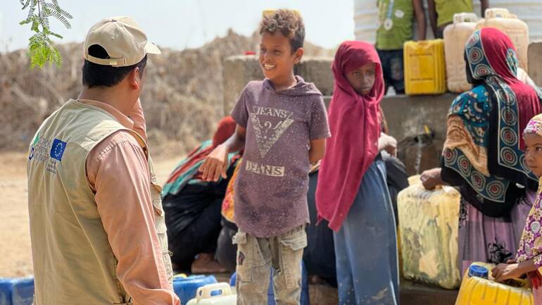 Ein Mitarbeiter von Aktion gegen den Hunger spricht mit Kindern, die gerade frisches Wasser abholen.