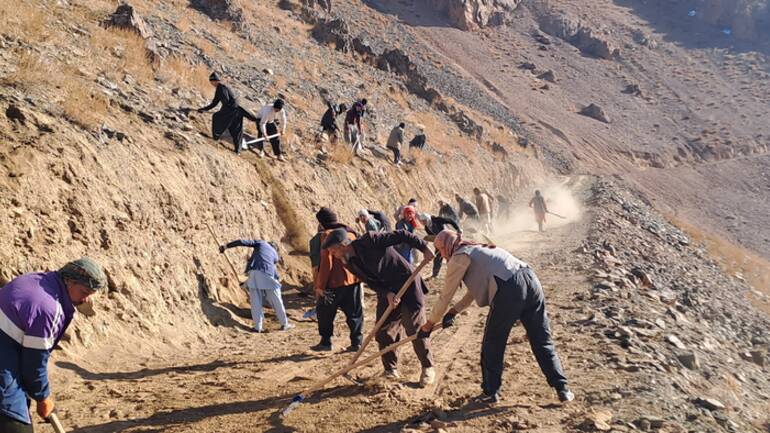 Unsere lokalen Teams in Afghanistan arbeiten mit Schaufeln und Rechen an der Befestigung einer Straße, die durch das Hochland von Daykundi führt.