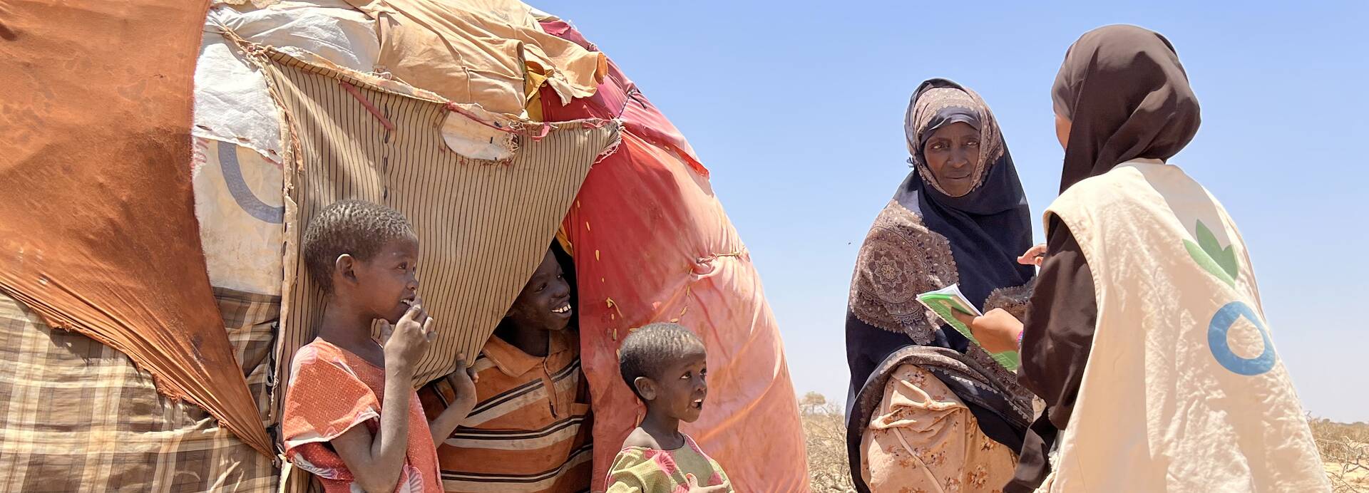 Mitarbeitende von Aktion gegen den Hunger sprechen mit einer Mutter und ihren Kindern vor ihrem Zelt in Somalia. Mitarbeitende von Aktion gegen den Hunger sprechen mit einer Mutter und ihren Kindern vor ihrem Zelt in Somalia.