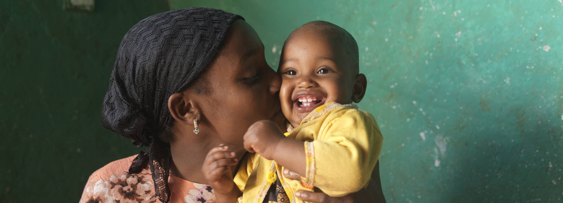 Eine Mutter drückt ihrem lachenden Baby einen Kuss auf die Wange Eine Mutter drückt ihrem lachenden Baby einen Kuss auf die Wange
