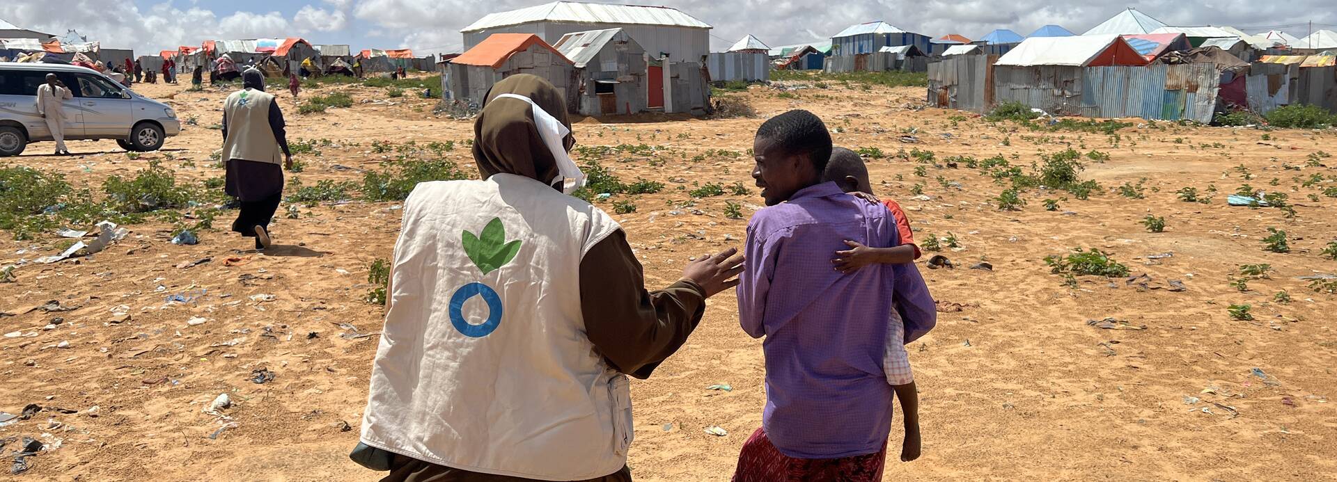 Eine Mitarbeiterin von Aktion gegen den Hunger in Somalia begleitet einen Vater mit Kind auf dem Arm durch ein Camp. Eine Mitarbeiterin von Aktion gegen den Hunger in Somalia begleitet einen Vater mit Kind auf dem Arm durch ein Camp.