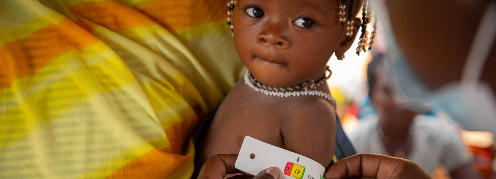 Kind auf dem Arm mit einem MUAC-Band um. Kind auf dem Arm mit einem MUAC-Band um.