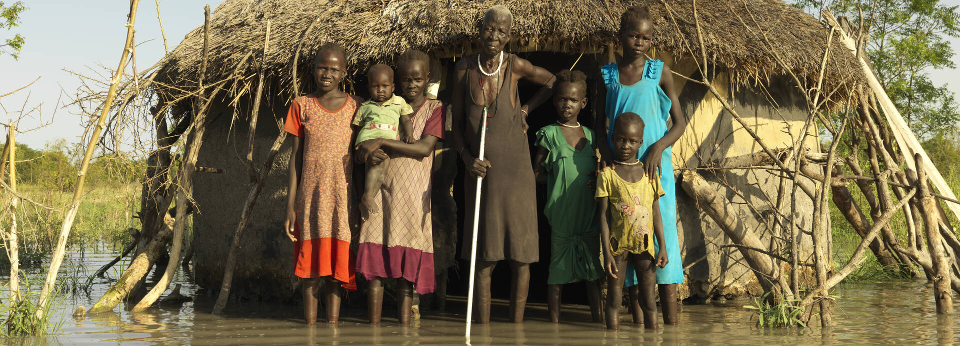 Nyabiele aus dem Südsudan steht mit ihrer Familie vor einer überfluteten Hütte im Dorf Nyabiele aus dem Südsudan steht mit ihrer Familie vor einer überfluteten Hütte im Dorf