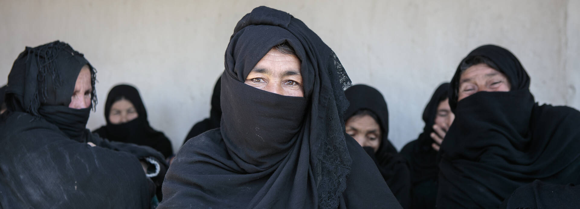 Frauen aus Afghanistan in schwarzen Tüchern sitzen zusammen, die Frau in der Mitte schaut in die Kamera
