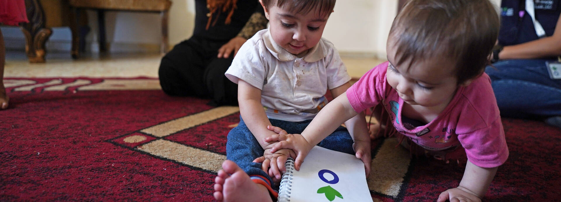 Danas Zwillinge Nagham und Akram spielen mit einem Notizbuch von Aktion gegen den Hunger auf einem Teppich in ihrer Unterkunft im Südlibanon. Danas Zwillinge Nagham und Akram spielen mit einem Notizbuch von Aktion gegen den Hunger auf einem Teppich in ihrer Unterkunft im Südlibanon.