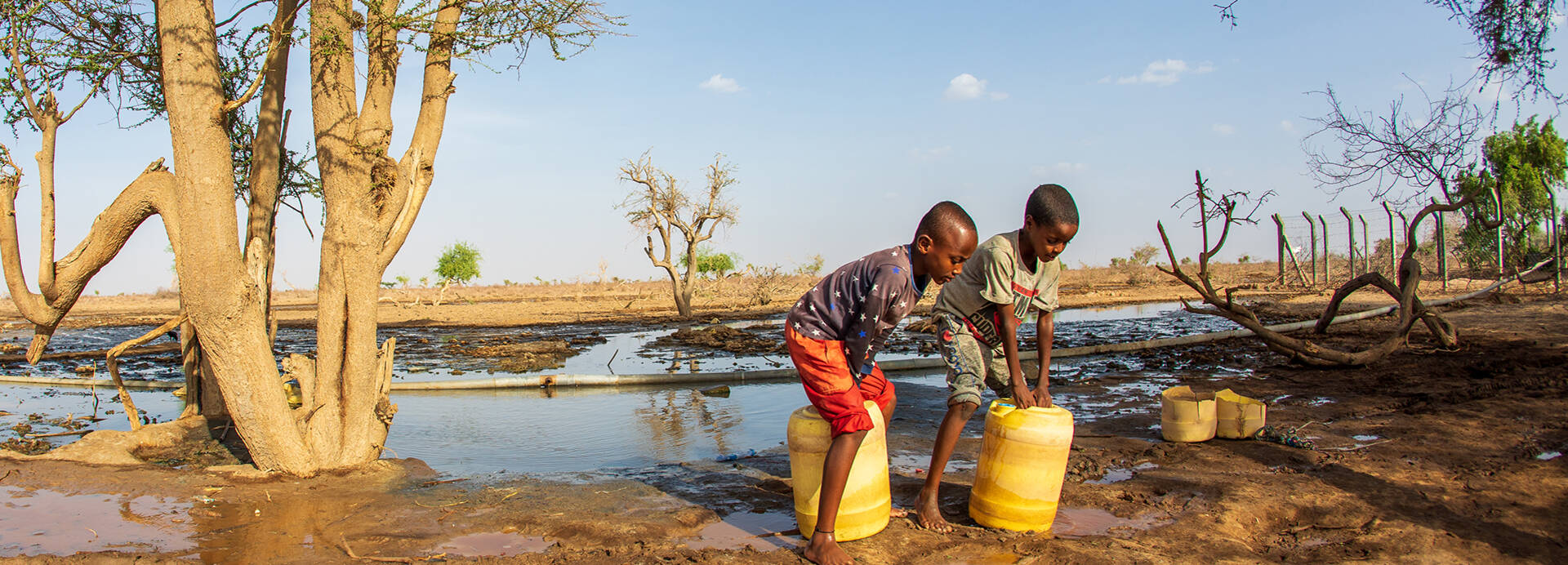 Zwei Kinder aus Kenia beim Wasser holen mit gelben Kanistern Zwei Kinder aus Kenia beim Wasser holen mit gelben Kanistern