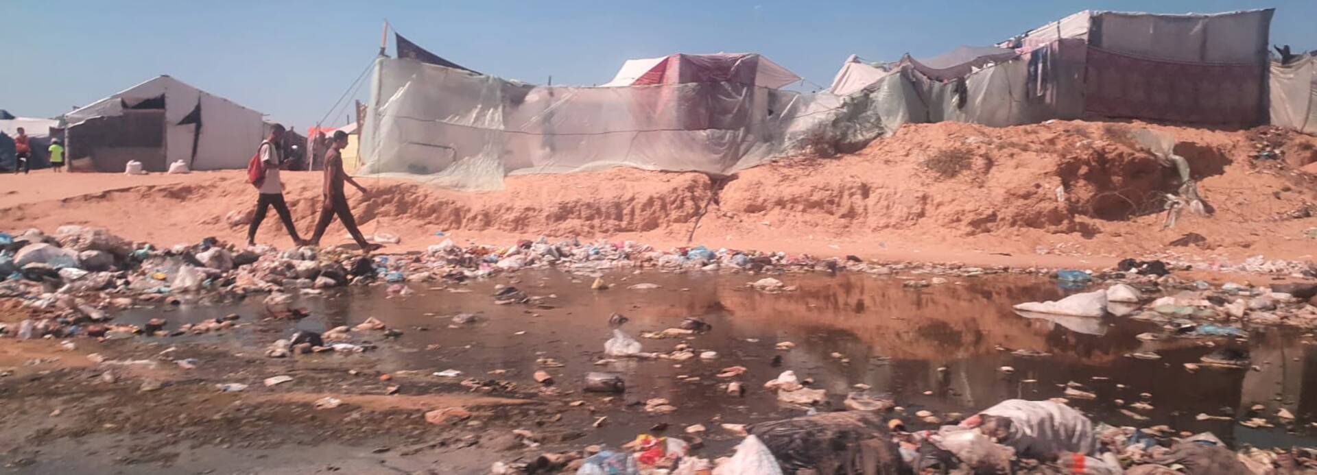 Zwei Jugendliche laufen an einer zerstörten Zeltstadt in Gaza vorbei.