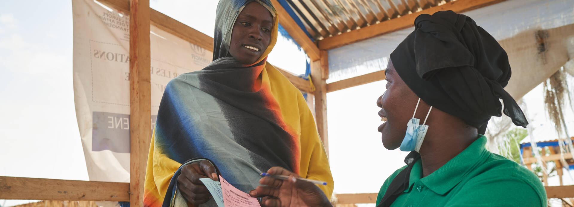 Eine Mitarbeiterin gibt einer Frau aus dem Tschad Bescheinigungen.