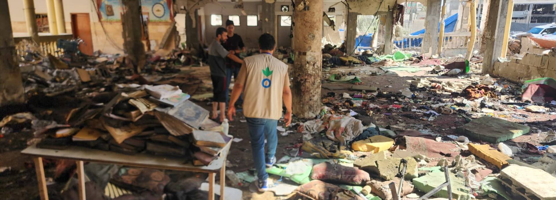 Ein Mitarbeiter steht mit weiteren Menschen in einem zerstörten Schulgebäude in Gaza Stadt.