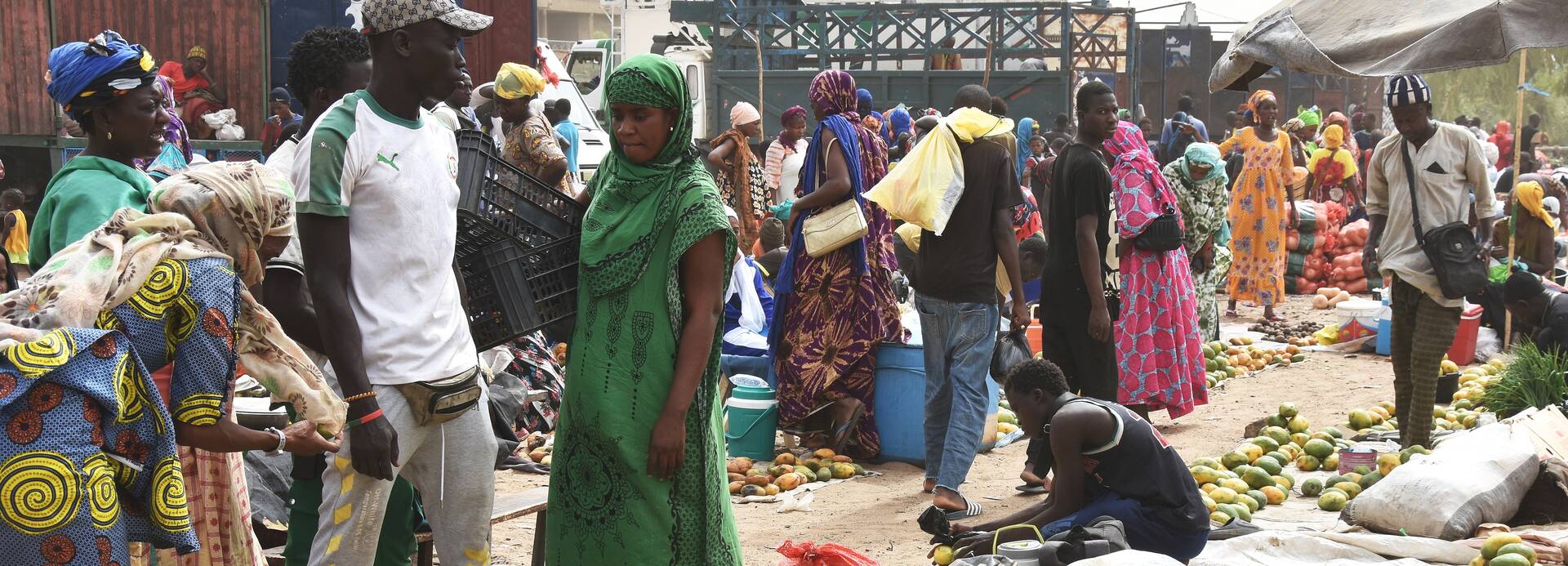 Ein Markt im Senegal, im Vordergrund Früchte, viele Menschen sind anwesend.