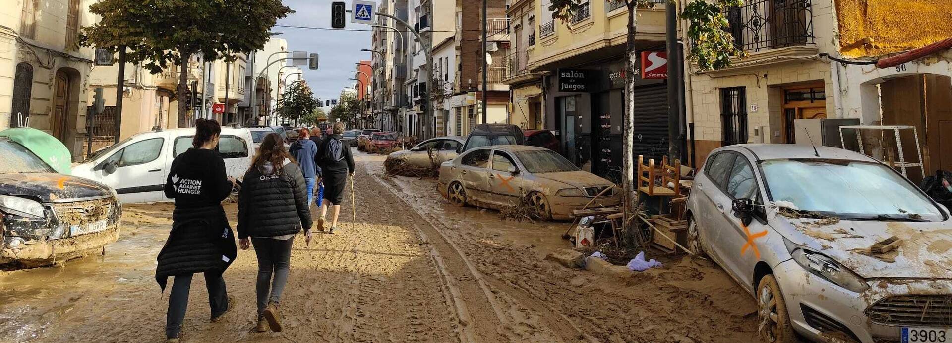 Mitarbeitende von Aktion gegen den Hunger laufen durch eine schlammige Straße in Valencia.