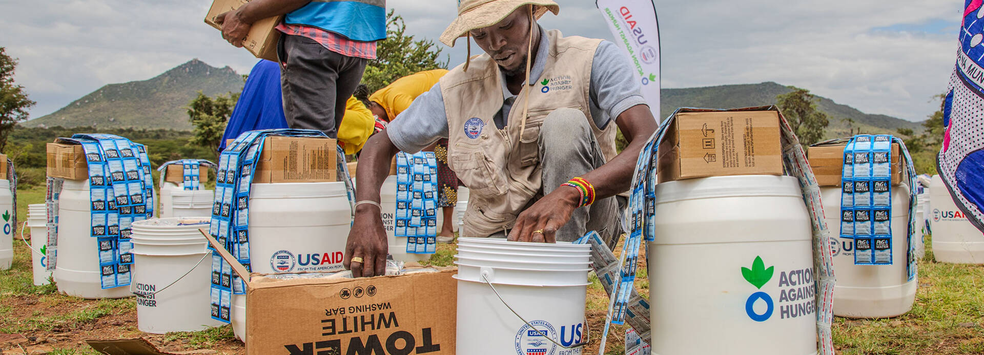 Einer unserer Mitarbeiter in Kenia füllt Hilfsgüter in Eimer mit der Aufschrift "Aktion gegen den Hunger" und "USAID".