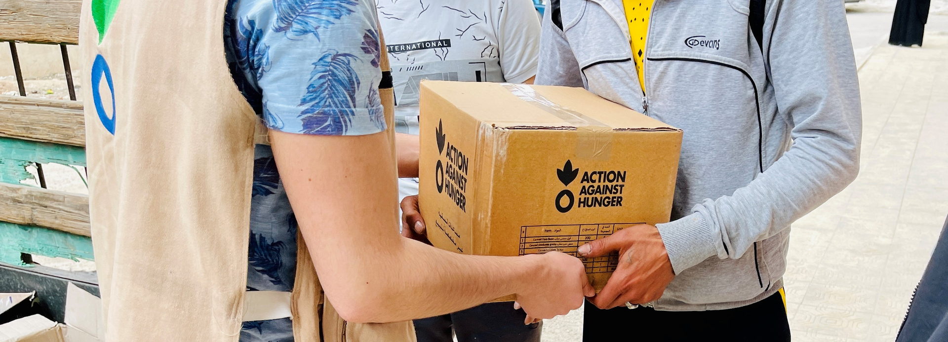 Ein Mitarbeiter von Aktion gegen den Hunger übergibt in Syrien ein Paket mit Nahrungsmitteln an einen jungen Mann.