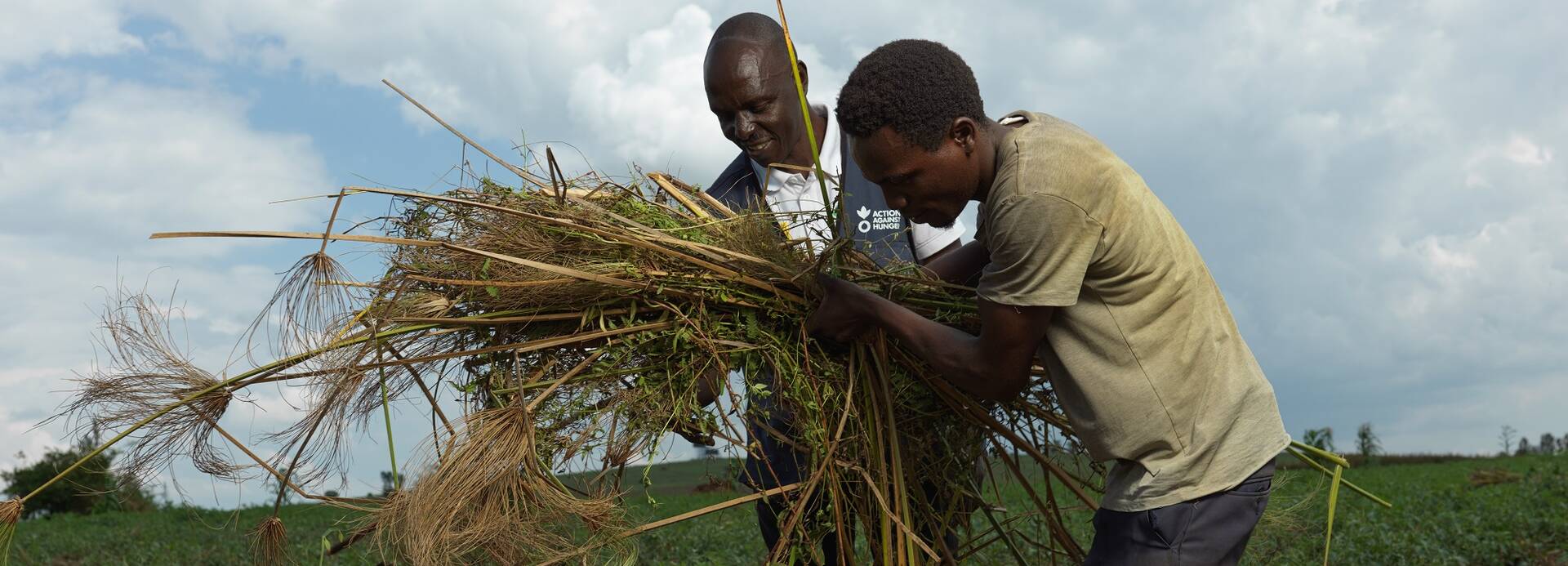 Ein Mitarbeiter von Aktion gegen den Hunger und ein Programmteilnehmer aus Uganda bedecken Ackerboden mit Mulch.