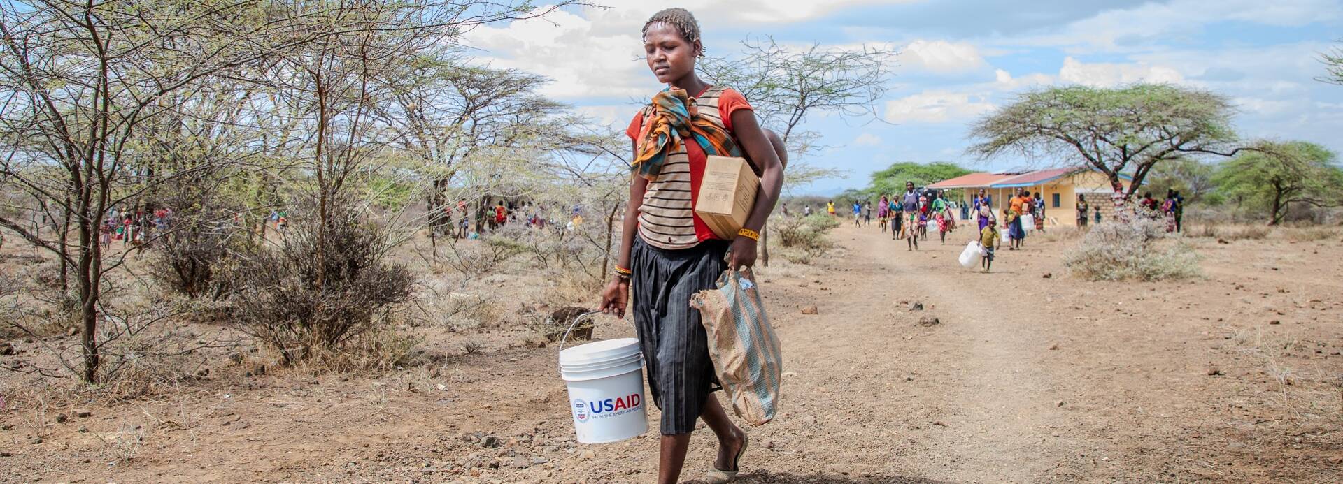 Eine Frau trägt einen Wasserkanister mit der Aufschrift "USAID".