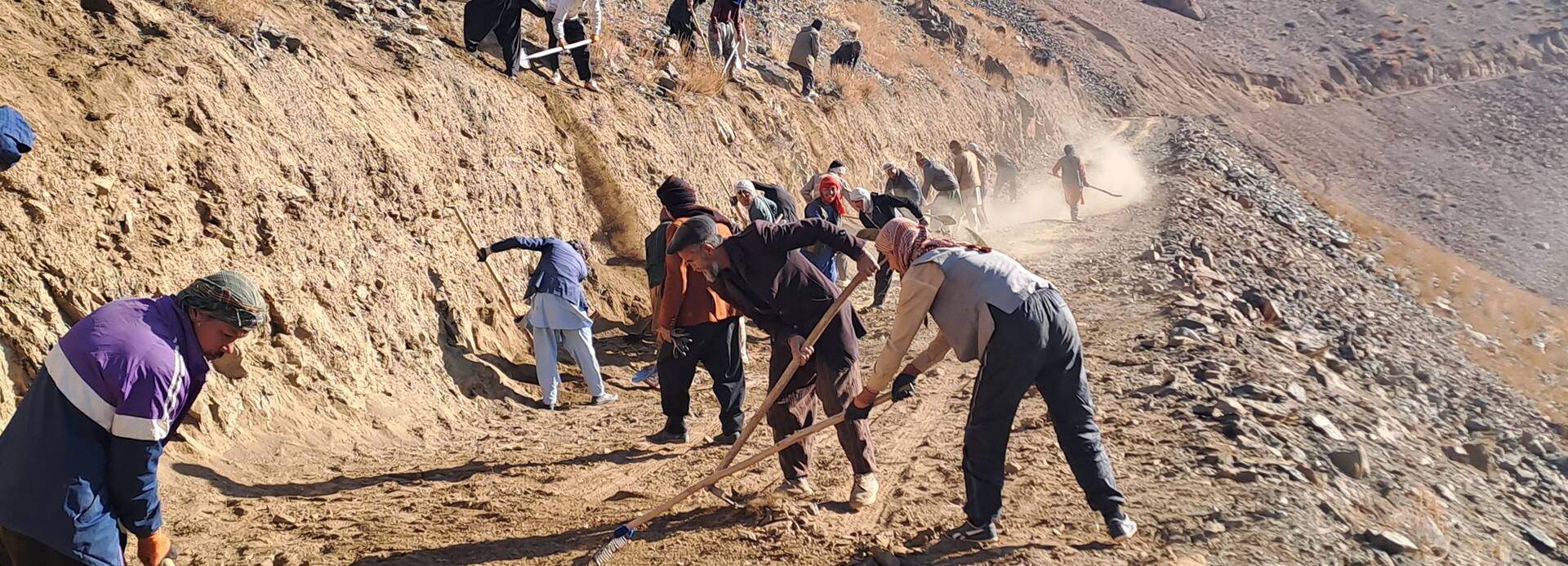 Unsere lokalen Teams in Afghanistan arbeiten mit Schaufeln und Rechen an der Befestigung einer Straße, die durch das Hochland von Daykundi führt.
