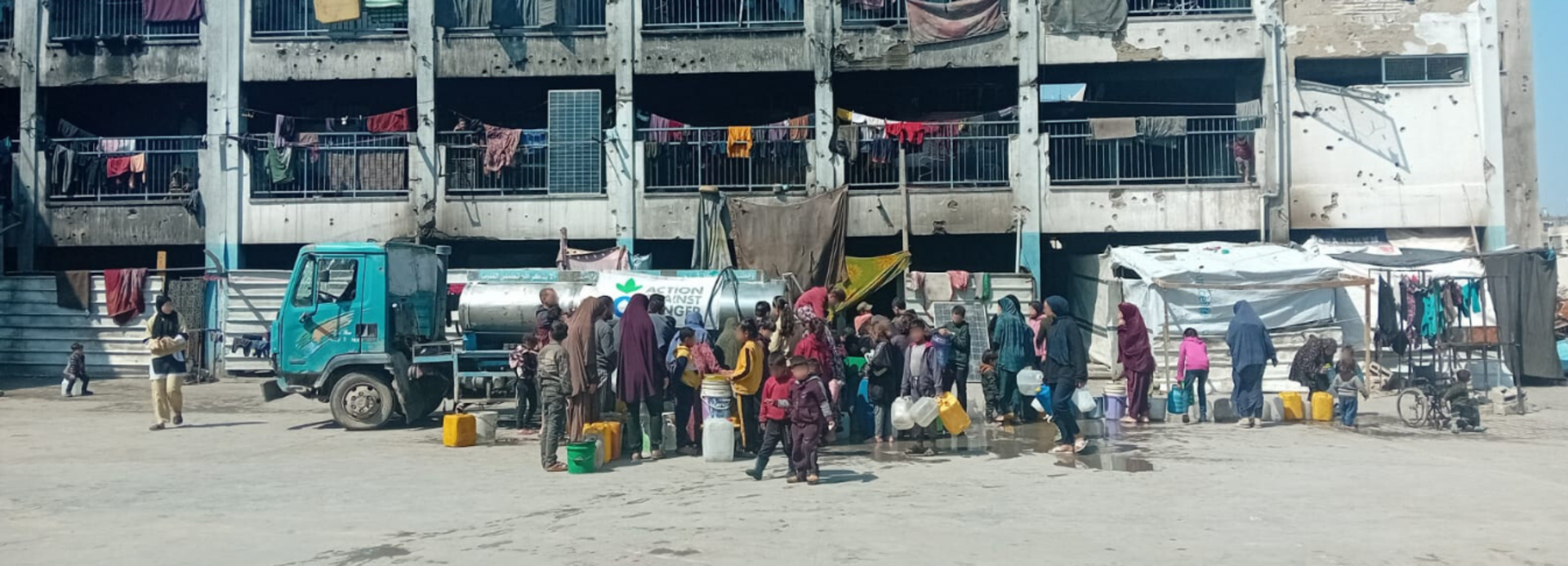 Menschen in Gaza stehen vor einem beschädigten Gebäude für Trinkwasser an.