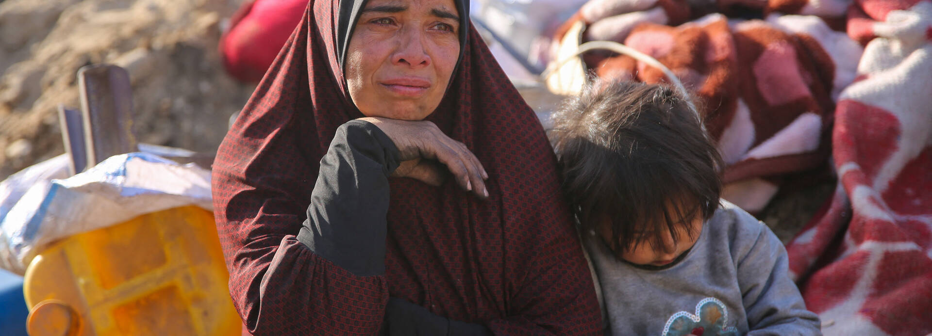 Eine Frau und ein Kind sitzen auf Decken im zerstörten Gazastreifen