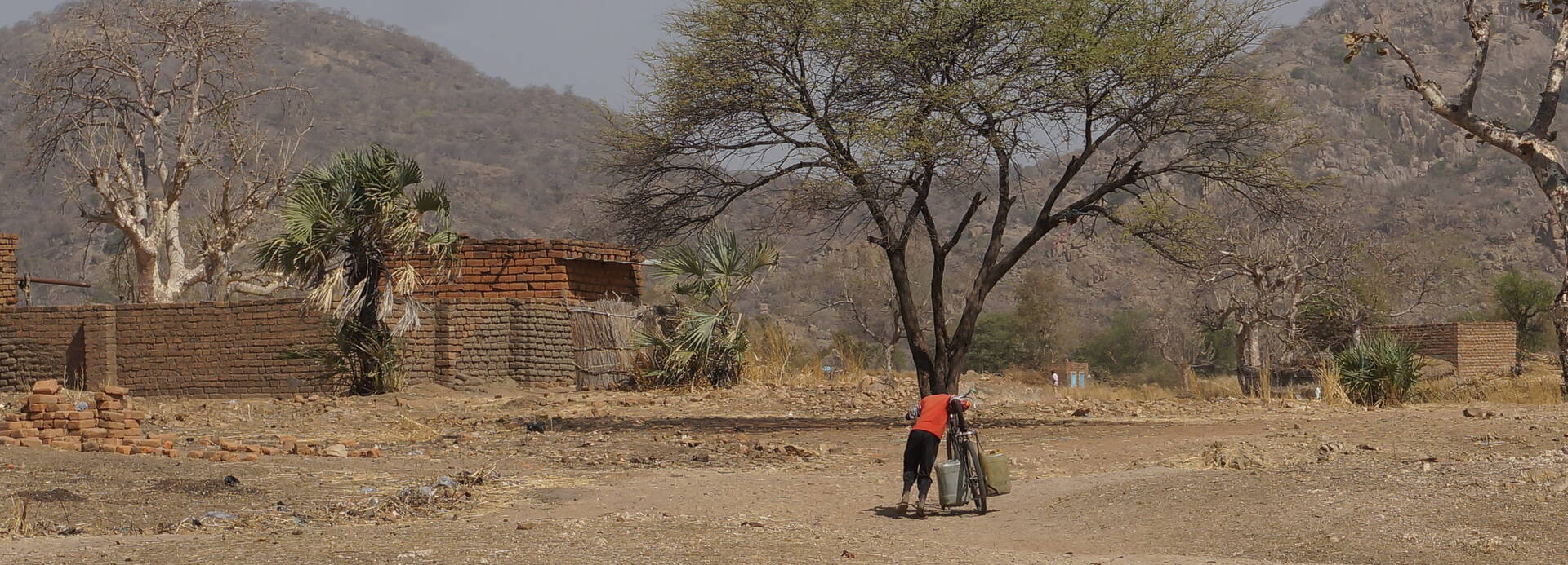 Eine Person schiebt ein Fahrrad in einer kargen ländlichen Umgebung in Süd-Kurdufan, Sudan.