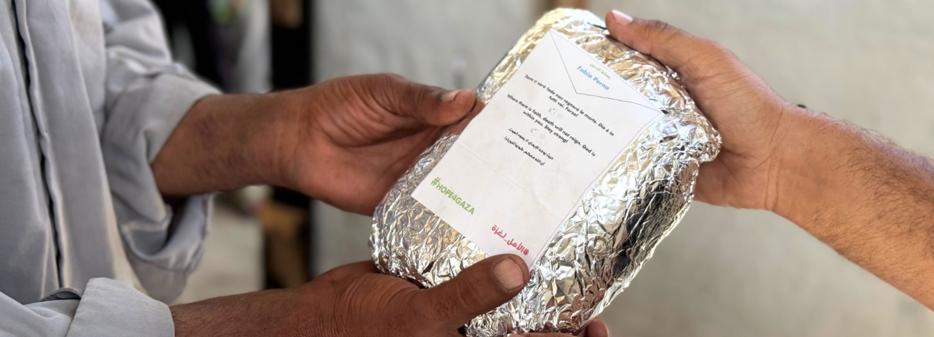 Ein Mitarbeiter von Aktion gegen den Hunger übergibt eine warme Mahlzeit, auf deren Packung eine Botschaft der Hoffnung steht.