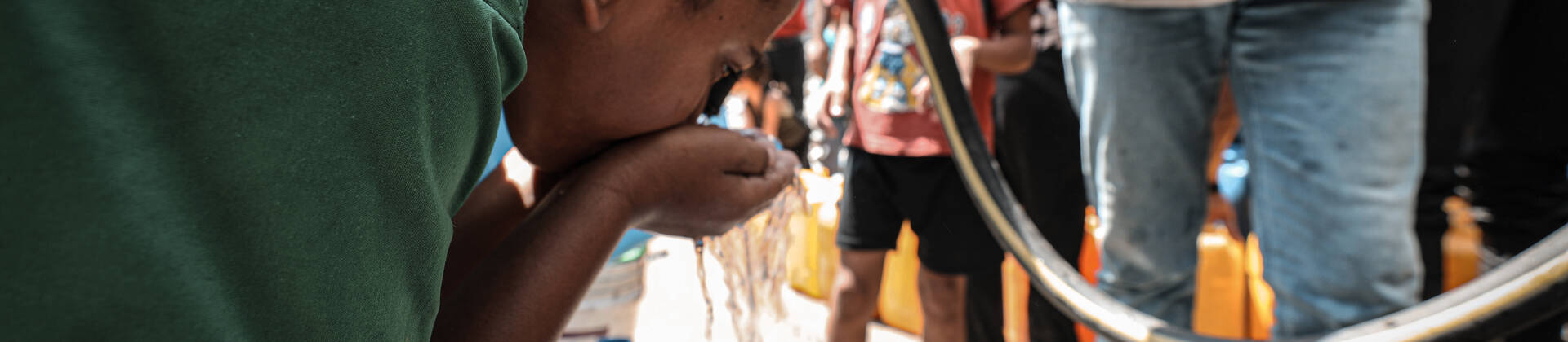 Ein Kind trinkt im Norden Gazas frisches Wasser aus einem Schlauch, den ein Mitarbeiter von Aktion gegen den Hunger hält.