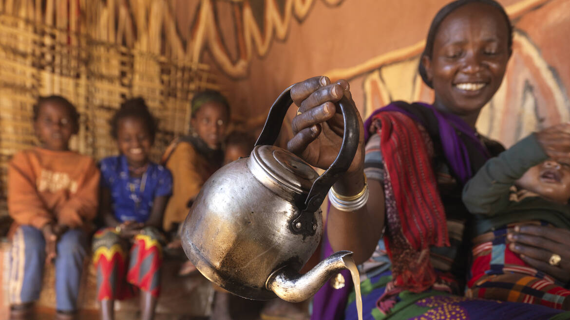 Frau gießt Tee ein und hält Baby im Arm