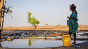 Eine Frau steht in einer trockenen Landschaft in Kenia am Rande eines Wasserlochs.