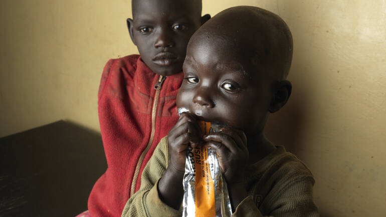 Chepengat und ihre Schwester mit Erdnusspaste Chepengat isst Erdnusspaste, ihre Schwester sitzt hinter ihr