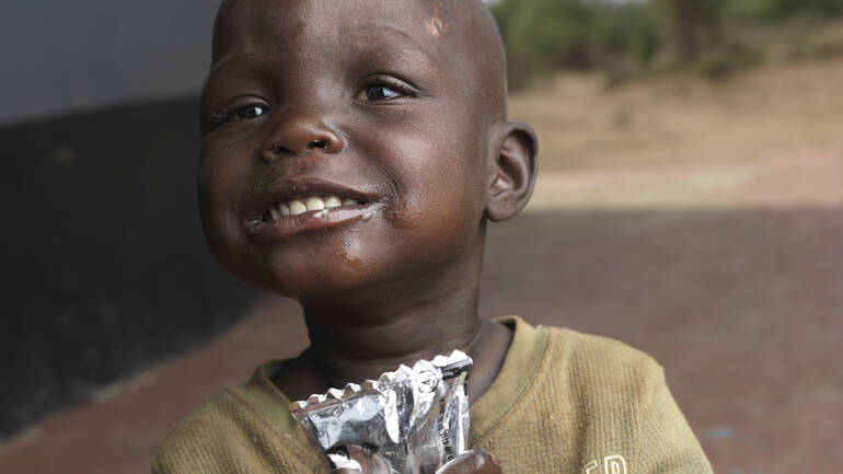 Chepengat mit Erdnusspaste Chepengat lächelt, in ihrer Hand ein Päckchen Erdnusspaste