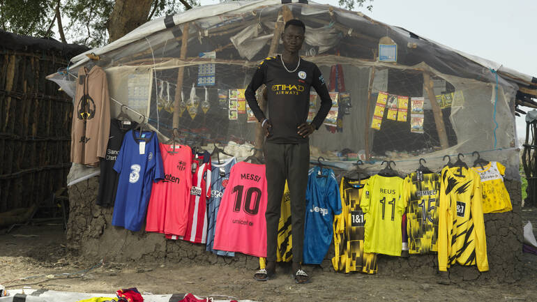 Gatwech Luok vor seinem Laden und den Fußballtrikots, die er verkauft