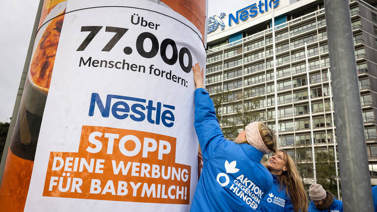 Mitarbeiterinnen von Aktion gegen den Hunger befestigen ein Plakat zum Erfolg der Petition vor der Nestlé-Zentrale in Frankfurt am Main. Mitarbeiterinnen von Aktion gegen den Hunger befestigen ein Plakat zum Erfolg der Petition vor der Nestlé-Zentrale in Frankfurt am Main.