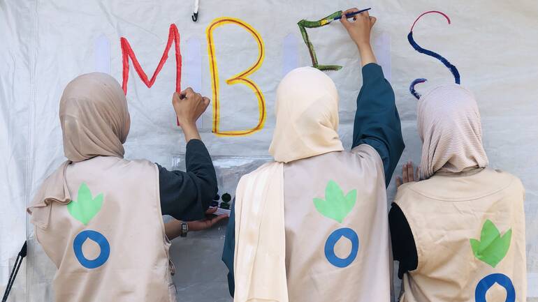 Mitarbeiterinnen von Aktion gegen den Hunger bemalen das Zelt mit den Buchstaben MBFS für Mother Baby Friendly Spaces.
