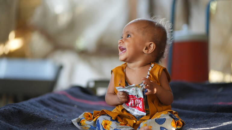 Eines der Kinder von Ali Ahmed im Gesundheitszentrum, lachend mit einer Packung RUTF in der Hand.