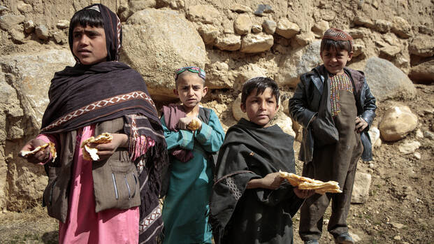 Die Hungerkrise wird sich in Ländern wie Afghanistan ausweiten Vier Kinder aus Afghanistan stehen mit Brot in der Hand auf Steinen.