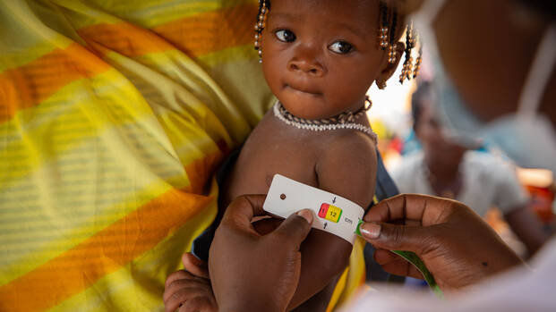 Kind auf dem Arm mit einem MUAC-Band um. 