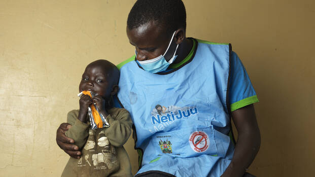 Erdnusspaste hat Chepengats Leben gerettet Chepengat sitzt mit einem Pfleger auf einer Liege, sie isst Erdnusspaste