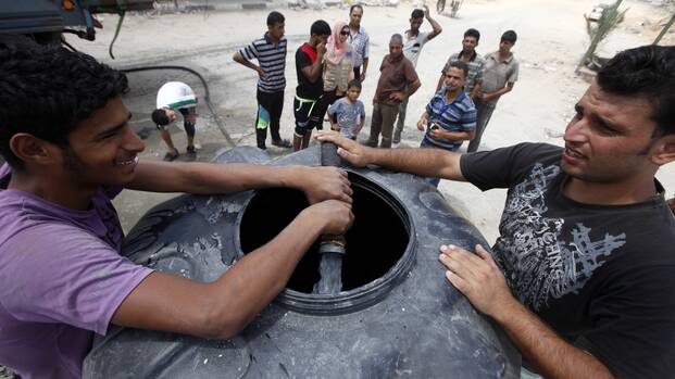 Während der Kämpfe mussten alle WASH-Aktivitäten ausgesetzt werden – es ist wichtig, diese nun in der Waffenruhe und darüber hinaus fortführen zu können, etwa um genügend Wasser bereitzustellen. Zwei Männer füllen einen Wassertank mit frischem Wasser, im Hintergrund stehen weitere Menschen