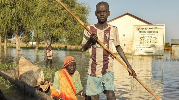 Ein Junge fährt mit einer älteren Frau in einem Baumstamm-Boot durch ein überflutetes Gebiet im Südsudan. Ein Junge fährt mit einer älteren Frau in einem Baumstamm-Boot durch ein überflutetes Gebiet im Südsudan.
