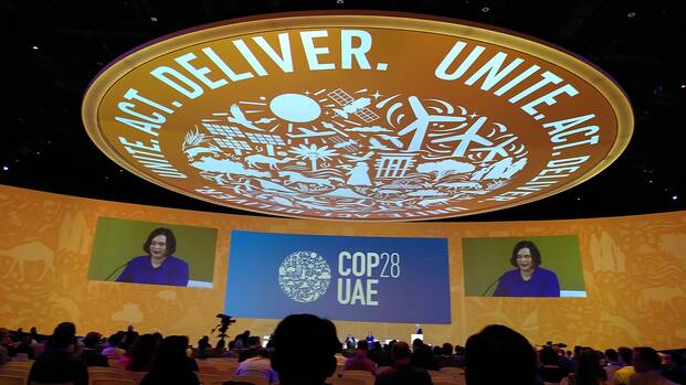 Im Plenarsaal der Klimakonferenz in Dubai sitzen die Vertreter*innen der Staaten und hören der Sprecherin vorne zu. Über allen wölbt sich eine große Kuppel mit der Aufschrift "Unite, Act, Deliver". Im Plenarsaal der Klimakonferenz in Dubai sitzen die Vertreter*innen der Staaten und hören der Sprecherin vorne zu. Über allen wölbt sich eine große Kuppel mit der Aufschrift "Unite, Act, Deliver".